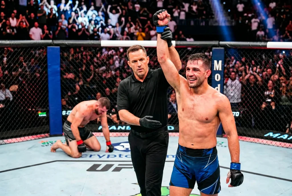 Schiedsrichter hebt den Arm eines siegreichen MMA-Kämpfers im Käfig nach Kampfende